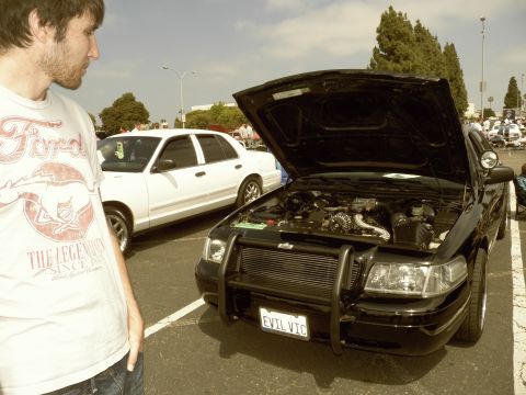 2003 Ford Crown Victoria - Black Crown Victoria with raised hood and push bar, plate reading EVIL VTC, beside a white Crown Vic