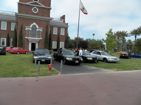 2003 Ford Crown Victoria - Black and silver Crown Victoria sedans on a lawn by a brick building flying a California flag