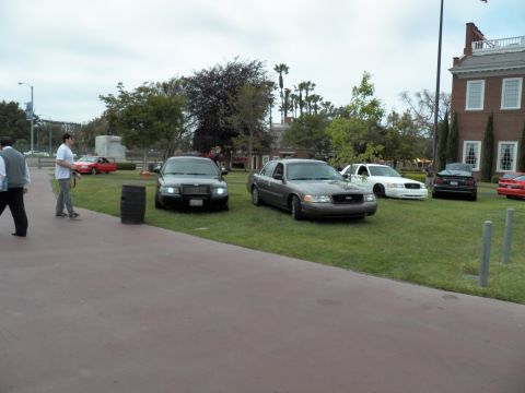 2003 Ford Crown Victoria - People stand on a walkway beside gray and black Crown Victoria sedans parked on a green lawn