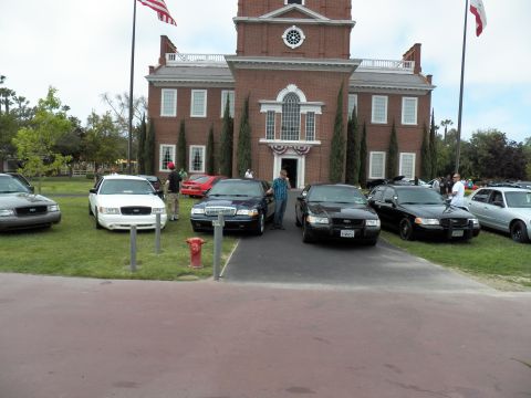 2003 Ford Crown Victoria - Crown Victoria sedans parked on a lawn facing a brick building with two flagpoles and bunting