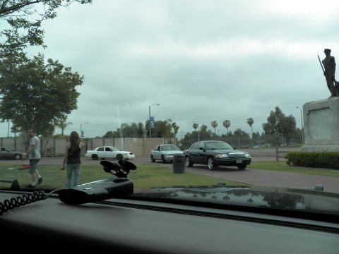 2003 Ford Crown Victoria - Dashboard and microphone frame a road where white and black sedans pass a soldier statue