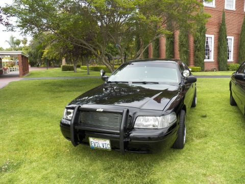 2003 Ford Crown Victoria - Black Crown Victoria with chrome push bar and Ford badge on a green lawn by a brick building