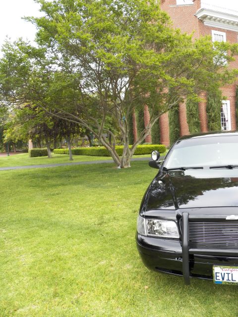 2003 Ford Crown Victoria - Front quarter of a black Crown Victoria sedan with grille guard, EVIL plate, on grass beside a red-brick building.
