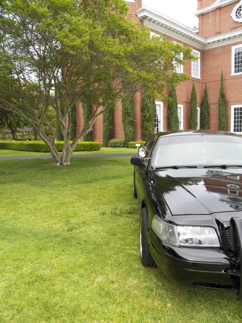 2003 Ford Crown Victoria - Close front-quarter view of a glossy black Crown Victoria sedan on a lawn, brick building and trees behind.