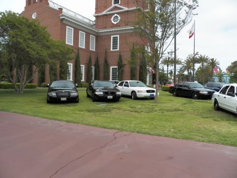 2003 Ford Crown Victoria - Cluster of Crown Victoria sedans on grass before a red-brick building, flags on a pole.