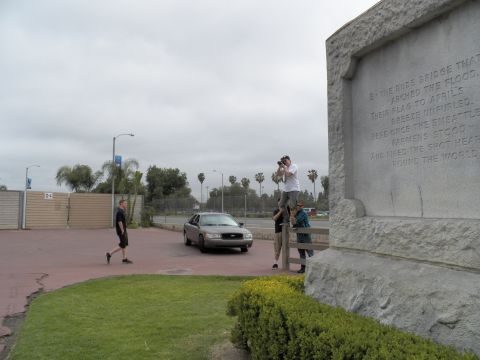 2003 Ford Crown Victoria - Engraved granite memorial reads BY THE RUDE BRIDGE THAT ARCHED THE FLOOD as a man takes photos nearby.