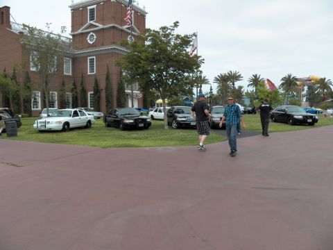 2003 Ford Crown Victoria - Men cross a maroon plaza as black and white Crown Victoria sedans sit on the lawn behind them.