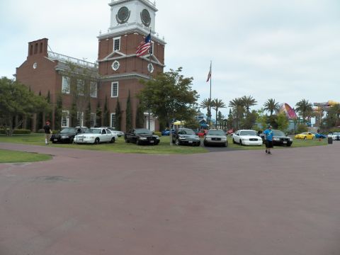 2003 Ford Crown Victoria - Row of police-style Crown Victoria sedans parked on grass in front of a brick clock-tower building.