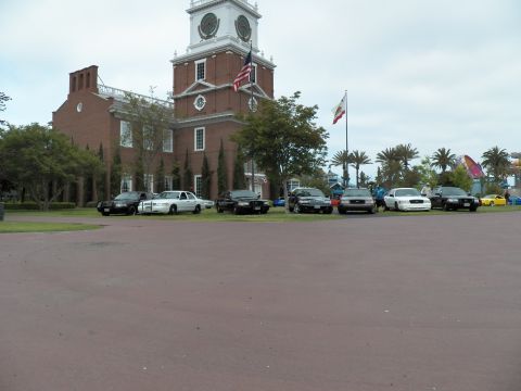 2003 Ford Crown Victoria - Black and white Crown Victoria sedans line up on a lawn fronting a brick clock-tower building.