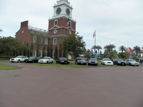 2003 Ford Crown Victoria - Row of black and white sedans parked on grass fronting a brick clock-tower building.