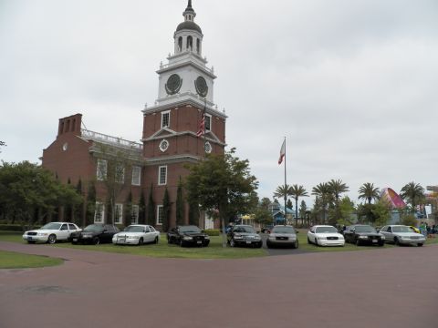 2003 Ford Crown Victoria - Panther-platform Ford and Mercury sedans gather on lawn near a colonial-style clock tower and flagpoles.