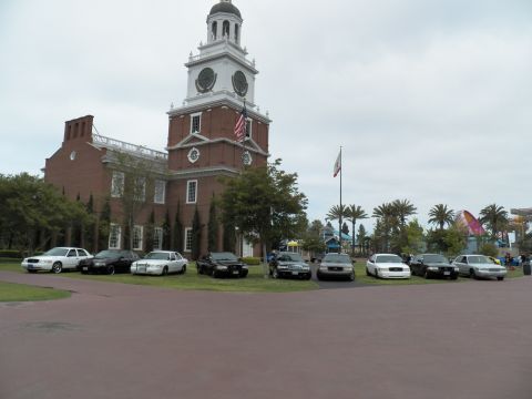 2003 Ford Crown Victoria - mix of black and white Ford sedans parks along the lawn beneath the clock tower and California flag.
