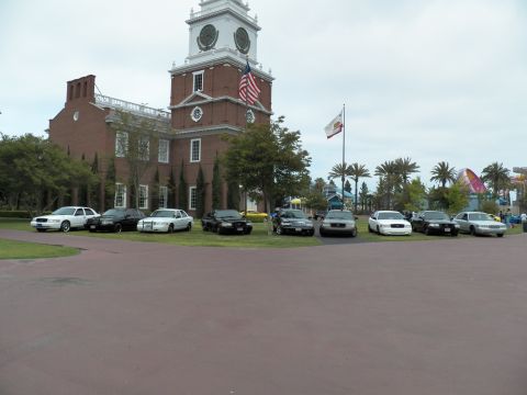 2003 Ford Crown Victoria - Panther-platform sedans line up on grass under the US and California flags at the clock-tower venue.