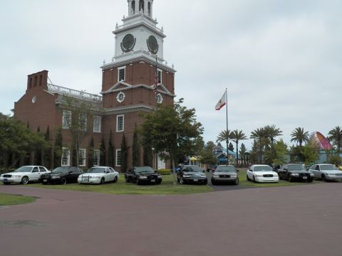 2003 Ford Crown Victoria - Black and white Panther-platform sedans park on grass beneath the colonial clock tower.