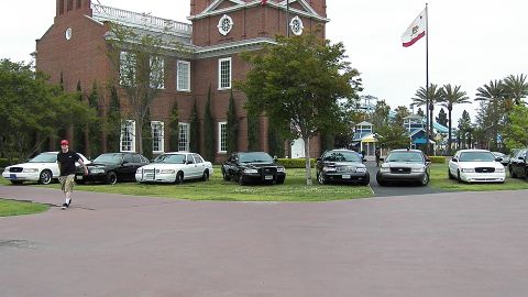 2003 Ford Crown Victoria - spectator crosses the lawn beside parked Panther-platform Ford and Mercury sedans.