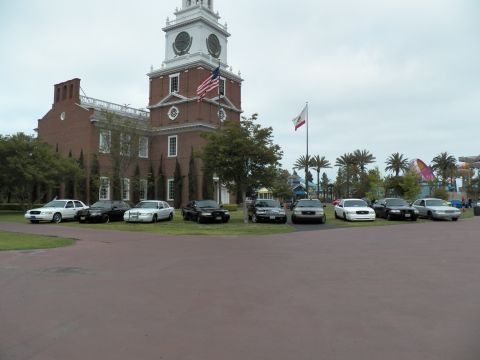 2003 Ford Crown Victoria - Panther-platform sedans park along the lawn beneath the colonial clock tower and palms.