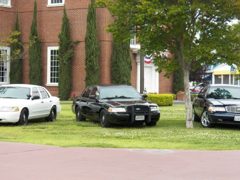 2003 Ford Crown Victoria - black Crown Victoria flanked by other sedans sits on lawn near red-white-blue bunting.