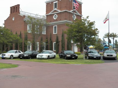 2003 Ford Crown Victoria - Panther-platform Ford and Mercury sedans line the lawn under the US flag and clock tower.