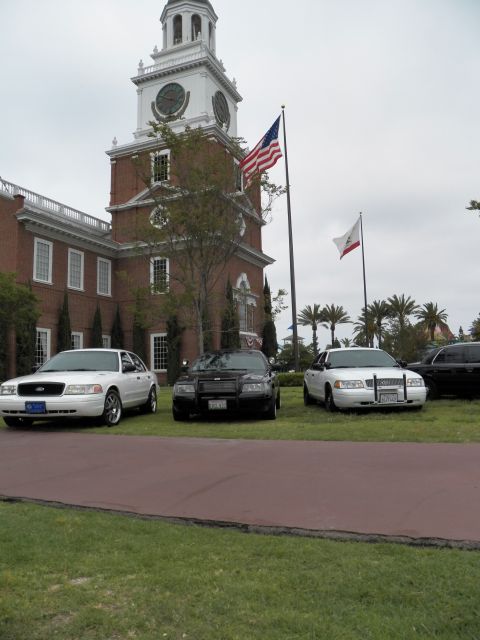 2003 Ford Crown Victoria - Crown Victorias park on lawn beneath the clock tower and twin flagpoles, portrait view.