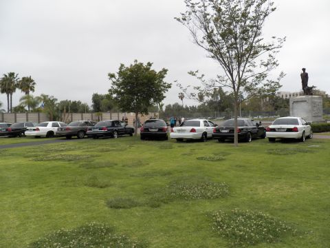 2003 Ford Crown Victoria - White, black and silver sedans lined on a lawn beside a soldier statue on a stone plinth