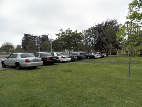 2003 Ford Crown Victoria - Silver sedan leading a parked lineup with a wooden roller coaster framework behind
