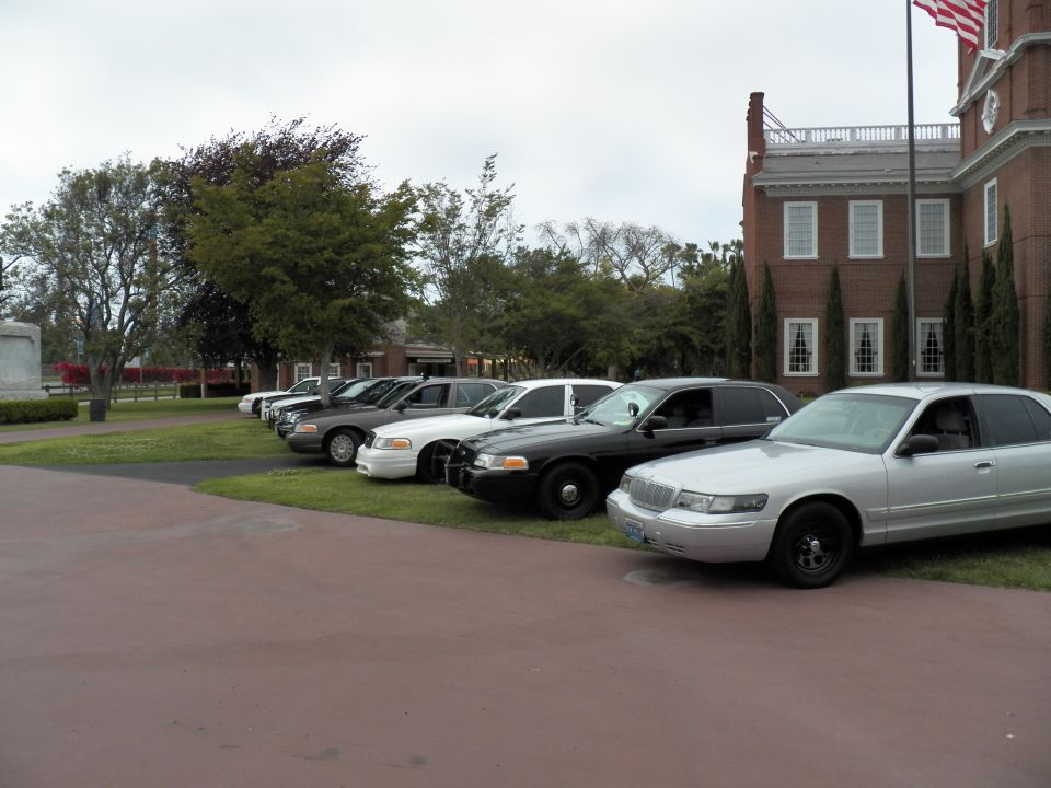 Silver Mercury Grand Marquis leading sedans parked by a brick building flying a US flag