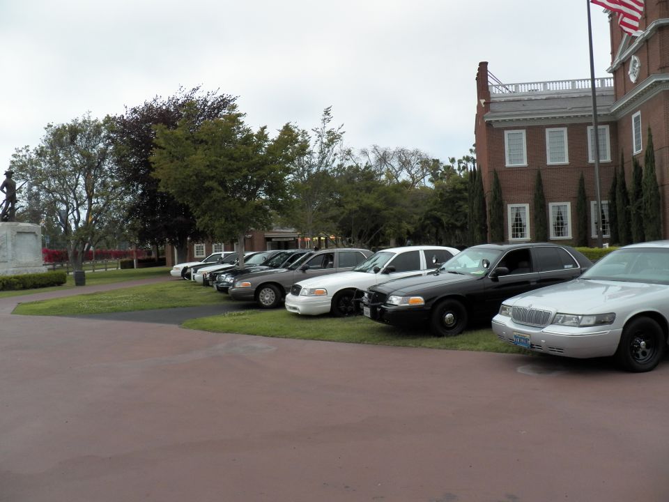Silver Mercury Grand Marquis ending a row of sedans by a brick building with US flag