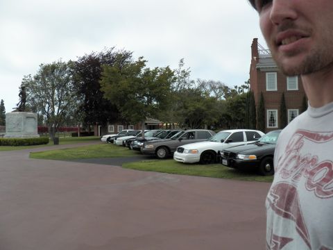 2003 Ford Crown Victoria - Bearded man wearing a gray Ford shirt with full-size sedans and brick hall behind him
