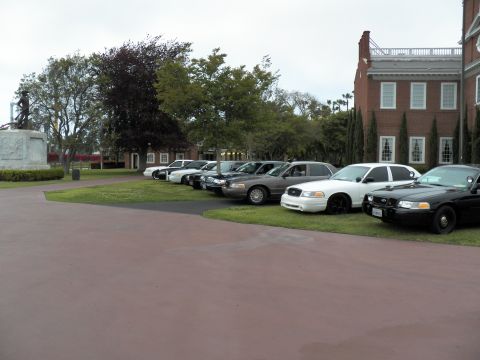 2003 Ford Crown Victoria - Lineup of full-size Ford sedans on a lawn near a statue and brick hall under gray sky
