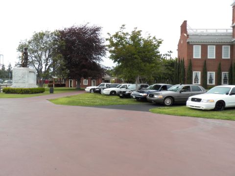 2003 Ford Crown Victoria - White, black and silver Ford sedans on a lawn beside a bronze statue and brick hall