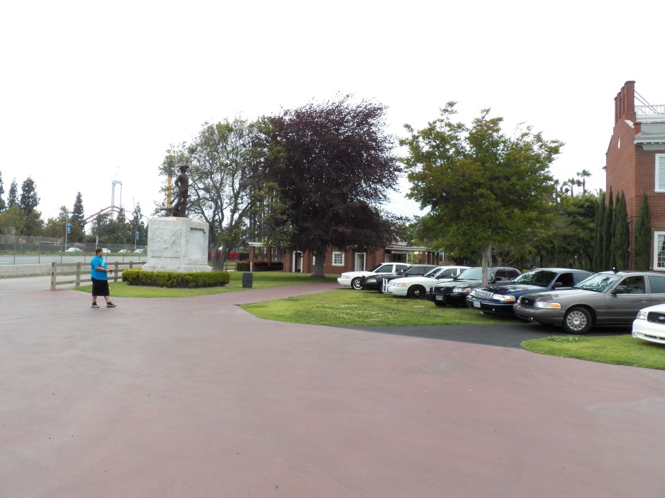 Person walking near a row of sedans parked by a statue and brick building