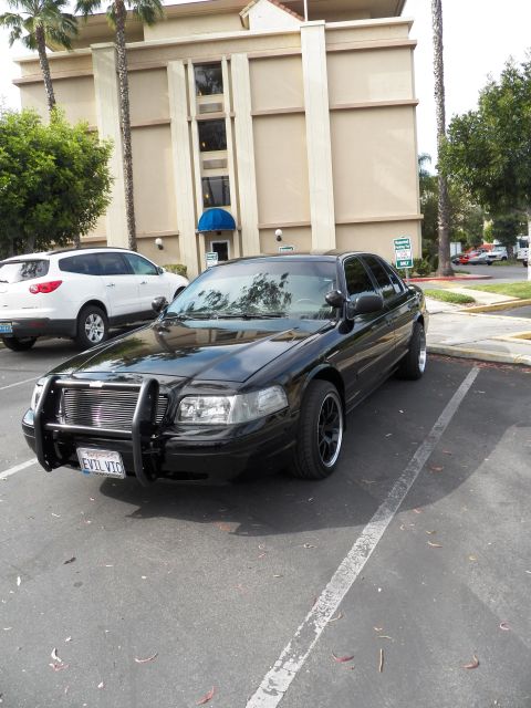 2003 Ford Crown Victoria - Front-quarter view of blacked-out Crown Vic, brush guard and dark wheels, white SUV beside it.