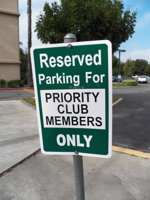 2003 Ford Crown Victoria - Reserved parking sign reading Priority Club Members Only, trees and lot behind.