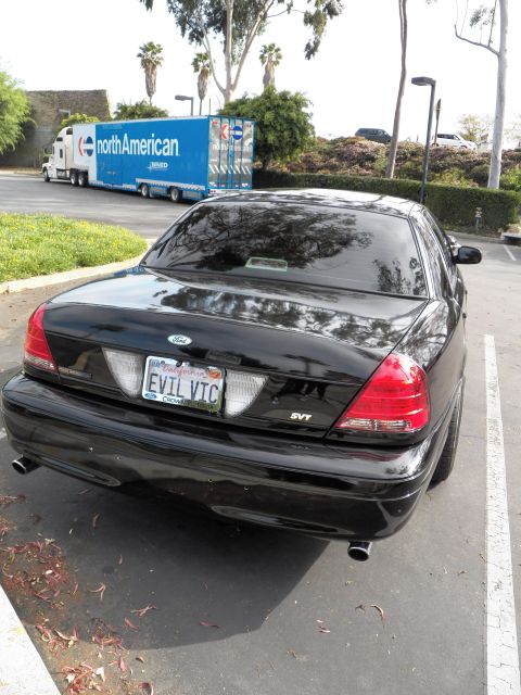 2003 Ford Crown Victoria - Rear-quarter of black Crown Vic, EVIL VIC plate and SVT badge, moving van behind.