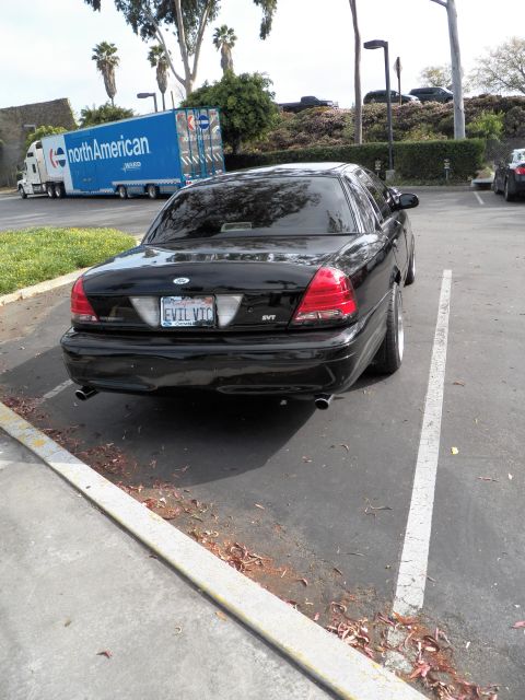 2003 Ford Crown Victoria - Blacked-out Crown Vic from behind, dual exhaust and SVT badge, North American van behind.