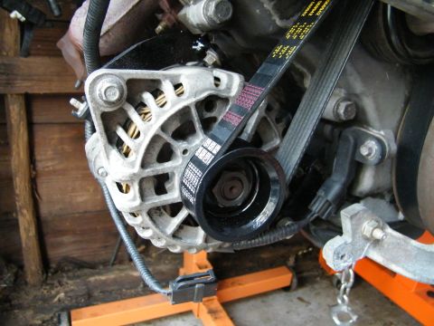 2004 Ford Crown Victoria - Close-up view of an engine's alternator and serpentine belt system, mounted on an engine stand.