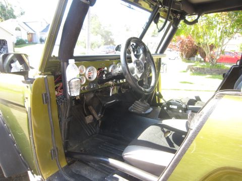 1974 Ford Bronco - The interior of a modified vehicle shows custom gauges and a roll cage, with a water bottle holder mounted to the dashboard.