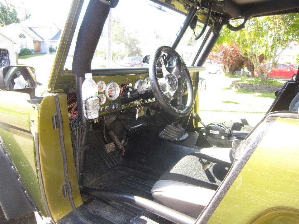 Green vehicle interior with aftermarket gauges, a chrome steering wheel, and a roll cage