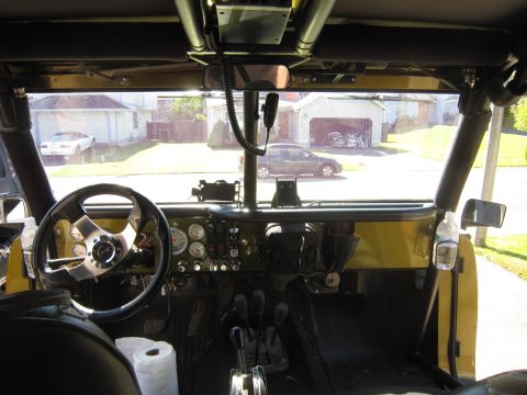 1974 Ford Bronco - The interior of a modified off-road vehicle is shown, with a view of the street and houses through the windshield.