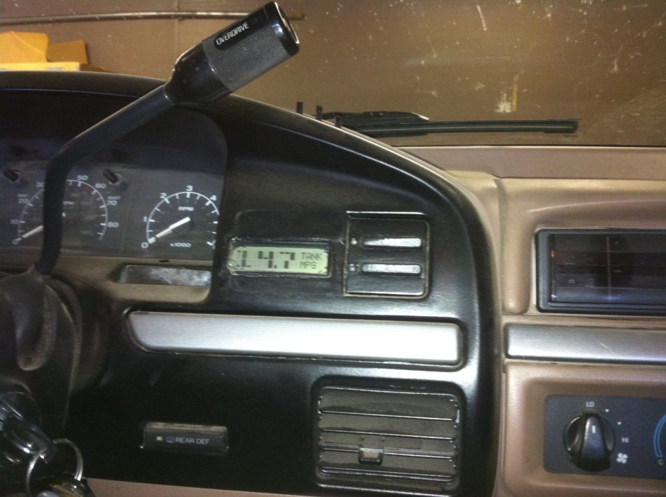 Dashboard interior with tachometer, speedometer, and digital display showing 14.7 MPG. Gear shifter with overdrive button is visible