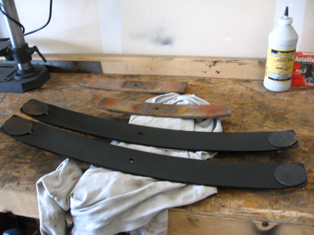 Freshly painted black leaf spring leaves on a workbench beside rusty old leaves