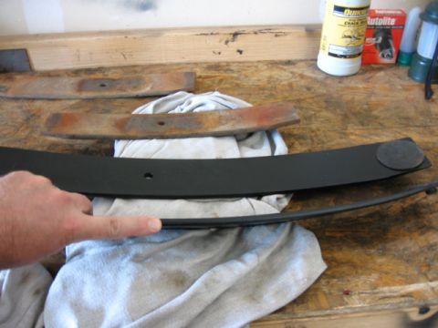 1995 Ford Bronco - A person points to a new black leaf spring, contrasting with older, rusty ones on a workbench.