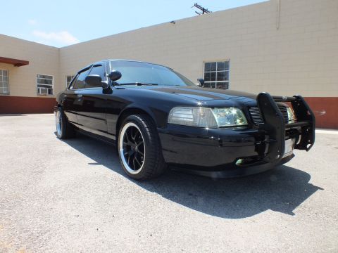 2003 Ford Crown Victoria - Front-quarter of murdered-out Crown Vic, brush guard and black wheels in bright sun.