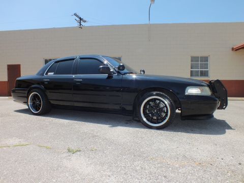 2003 Ford Crown Victoria - Side profile of lowered black Crown Vic, chrome-lip black wheels, tan building behind.