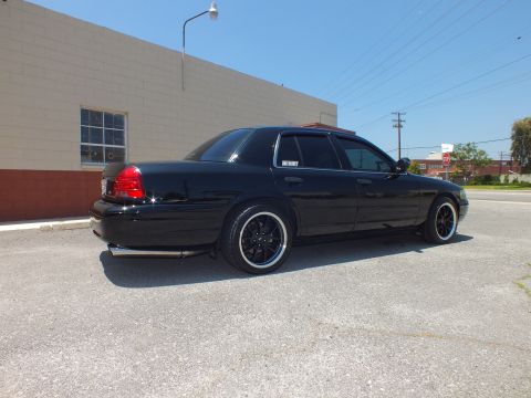 2003 Ford Crown Victoria - Rear-three-quarter of murdered-out Crown Vic, dual exhaust, power lines overhead.