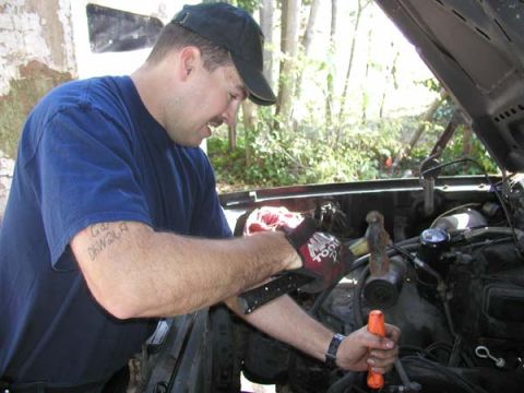 1988 Ford Bronco - Man performs maintenance on a vehicle's engine compartment, with tools in hand.