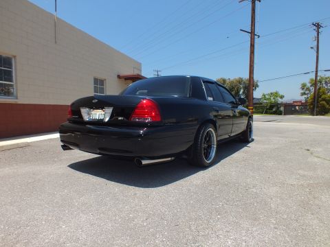 2003 Ford Crown Victoria - Rear-quarter of blacked-out Crown Vic, SVT badge and dual tips, utility pole behind.