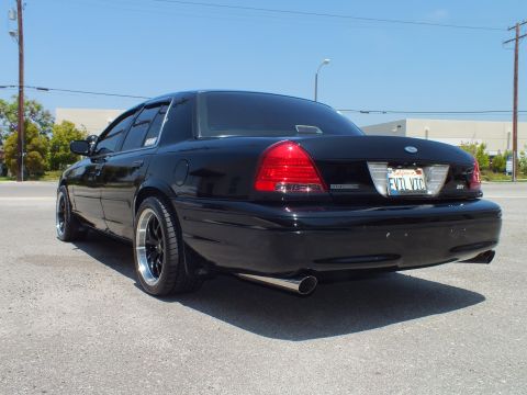 2003 Ford Crown Victoria - Rear-three-quarter of blacked-out Crown Vic with SVT badge, industrial backdrop.