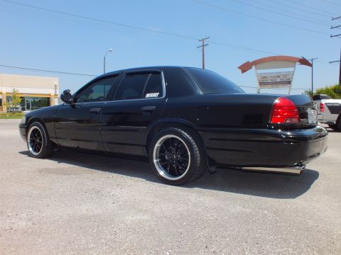 2003 Ford Crown Victoria - Rear-quarter profile of lowered black Crown Vic, dual exhaust, shop sign behind.