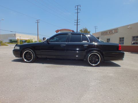 2003 Ford Crown Victoria - Side profile of murdered-out Crown Vic, tinted glass, Custom Mfg Co building behind.